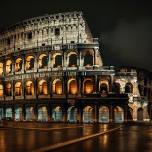 Het verlichte Romeinse Colosseum bij nacht met gouden licht dat door de bogen schijnt en natte straten die de reflecties weerkaatsen onder een donkere lucht.